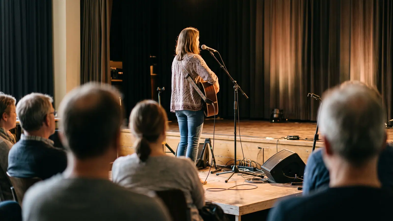 Musikerin mit Gitarre im Bühnenlicht, vom Publikum aus gesehen